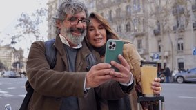 Happy senior couple using smartphone for navigation and pointing at something interesting while standing on city street with luggage and reusable coffee cup - Powered by Shutterstock - Get 15% off with code: PIKWIZARD15