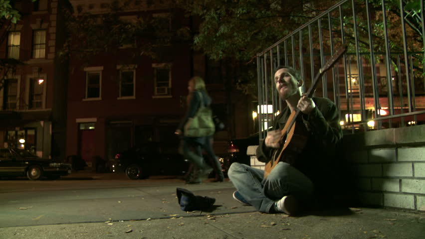 Young man playing a worn-out guitar on the night time streets of Manhattan, NY.