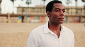 A young African American man in a white linen shirt stands on a beach, looking off into the distance. He reflects on life with a serious expression. - Powered by Shutterstock - Get 15% off with code: PIKWIZARD15