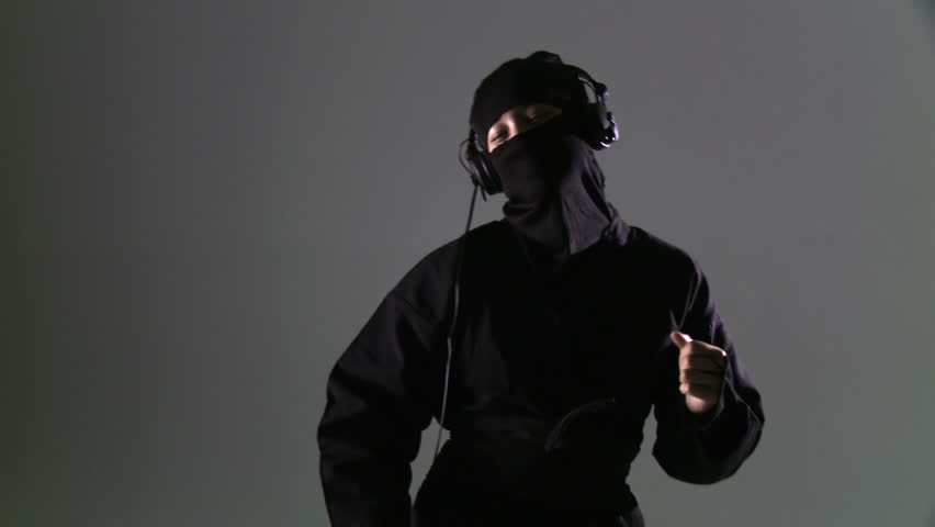 Ninja wearing headphones and dancing against a grey background. Midshot that