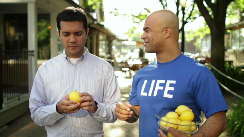 Man hands lemon back to a guy in a blue T-shirt that says 