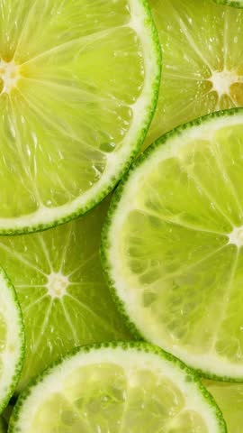 Lime slices closeup, fruits background top view. Rotate. Vertical footage