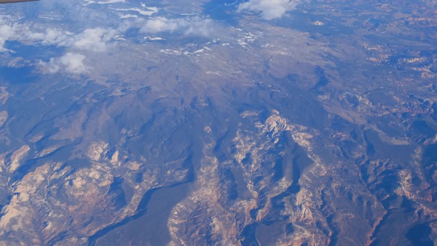The Grand Canyon showcases rocky mountains, deep valleys, and fluffy clouds under a clear blue sky. Aerial view