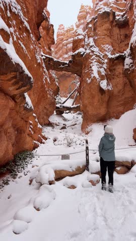 A female hiker surveys a winter landscape with stunning red rocks mercifully covered in fresh snow