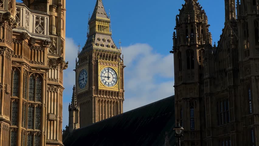 A sunny view of the Houses of Parliament and Big Ben in London, UK. Elizabeth Tower stands tall next to the River Thames in Great Britain. Tourist attraction in England.