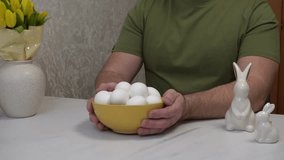 A man holds a bowl with white chicken eggs, preparing them for Easter coloring in different colors. - Powered by Shutterstock - Get 15% off with code: PIKWIZARD15