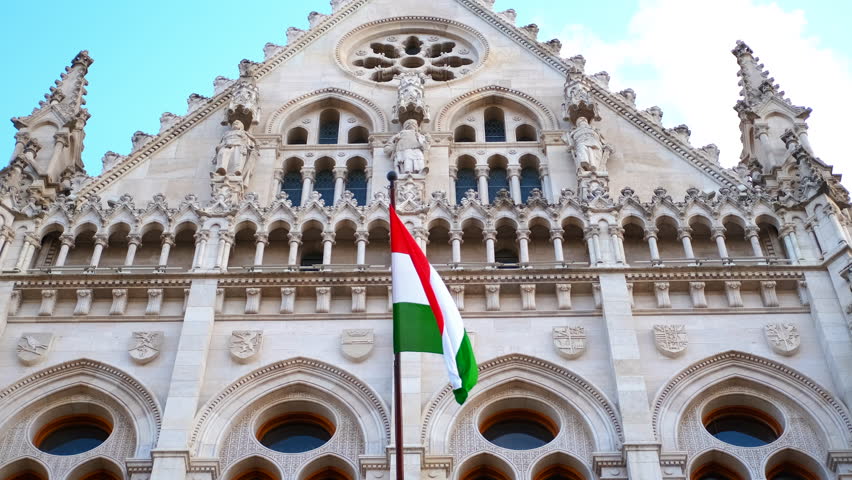 Hungarian flag waving in the wind in front of parliament building. The hungarian flag waves gracefully in the wind, the stunning backdrop of budapest