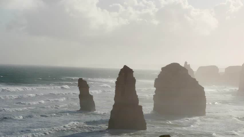 Stunning coastal rock formations under soft, golden light. Waves crash against the iconic Twelve Apostles along the Great Ocean Road