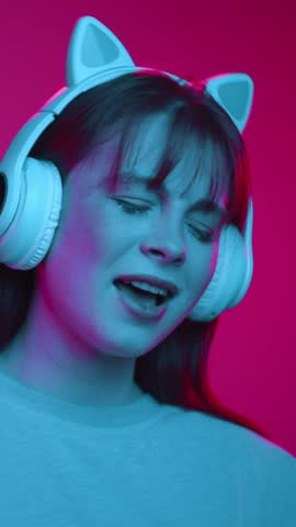 Happy Portrait of Dancing Woman in Funny Headphones Listening Music in Color Neon Light. One Playful Girl Hearing Singer Playlist and Singing Track with Feels. Technology Lover Uses Portable Head Set
