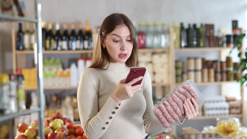 Girl scan QR-code on raw pork sausages package in store. Market visitor choose consider raw pork sausages semi finished products. Buyer pick up meat ware for bbq