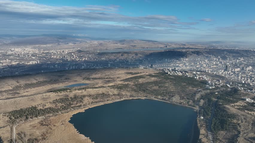 aerial view of a large city bordering a lake, with hills rolling in the background. The combination of urban development and natural scenery showcases the balance between city and nature