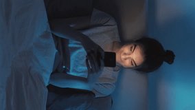Vertical video. Gadget night. Home internet. Online insomnia. Curious girl using mobile phone scrolling feed late in bed in dark bedroom. - Powered by Shutterstock - Get 15% off with code: PIKWIZARD15