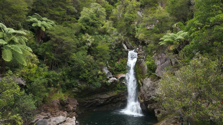 Beautiful cascading waterfall in lush greenery at Wainui Falls, Tasman Region, New Zealand, aerial pullback from pool