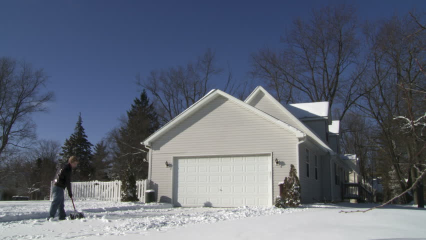 Teenager shovels snow from in front of a house in the Mid West, USA. Wide shot