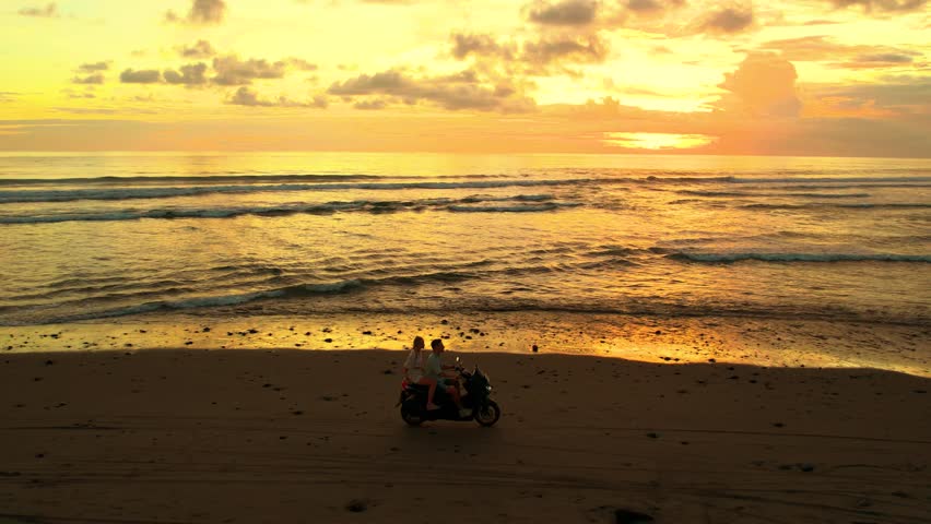 Couple riding a motorbike along the beach in Bali at sunset, with golden light reflecting on the ocean waves, feeling freedom and vacation vibe, independence. Motorcycle driving, moto trip