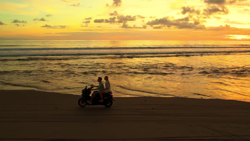 Freedom and vacation vibe when driving a motorbike along the beach in Bali at sunset, with ocean view, feeling independence. Motorcycle driving, moto trip, couple independent travelers ride bike.