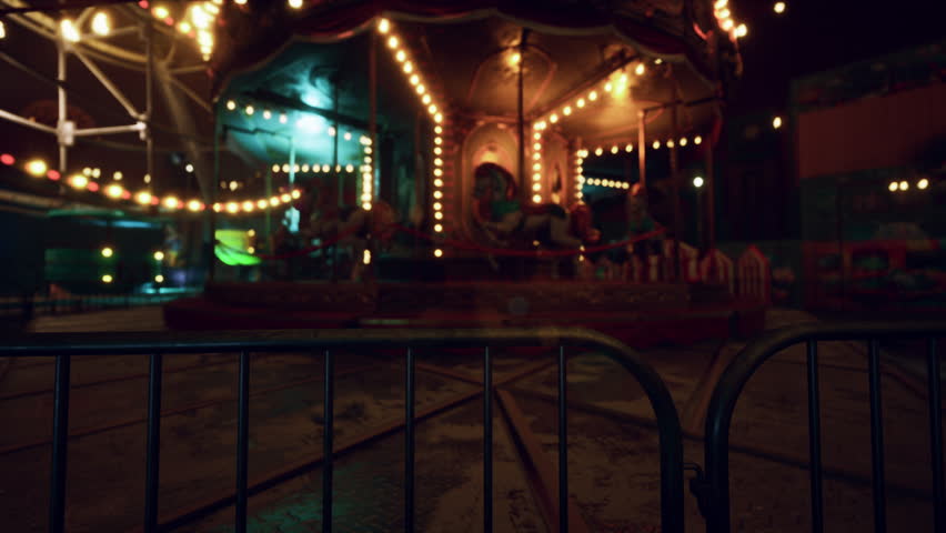 The amusement park sits in silence under the night sky, with empty rides and dimly lit pathways. The absence of visitors adds a haunting atmosphere to the once vibrant location.