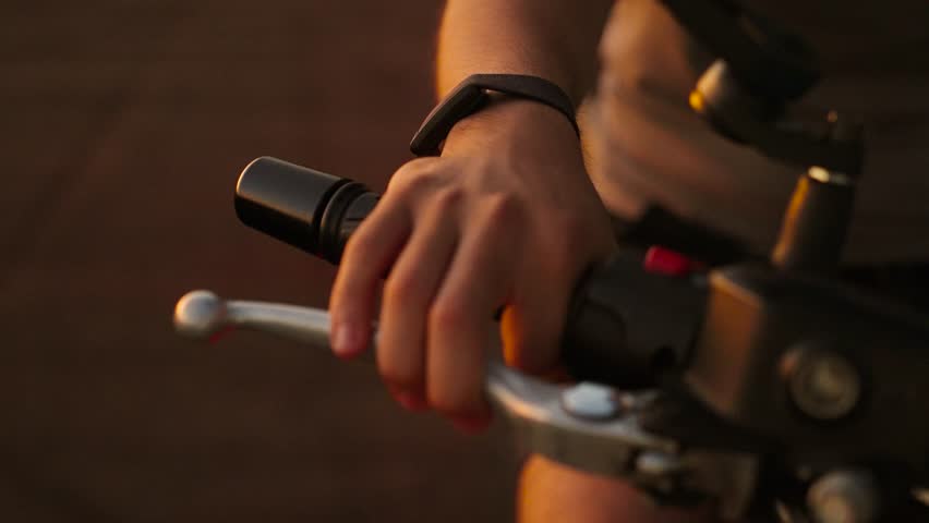 Close-up of a biker's hand gripping the gas lever of a motorcycle at sunset, starting the engine, adjusting gas on moto bike.