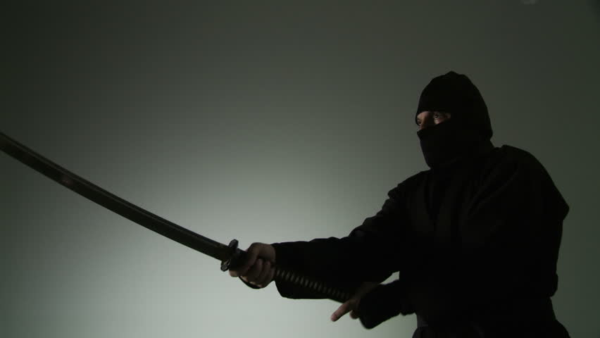 Medium close up of a masked ninja swinging a two-handed Japanese sword.