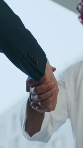 Vertical low angle shot of diverse businessmen shaking hands at indoor workspace