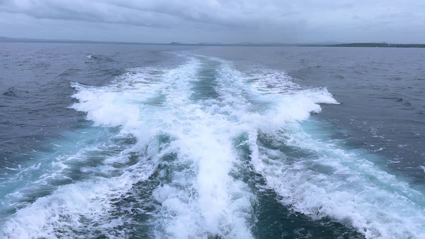 Boat wake foaming on the sea with a distant coastline in view