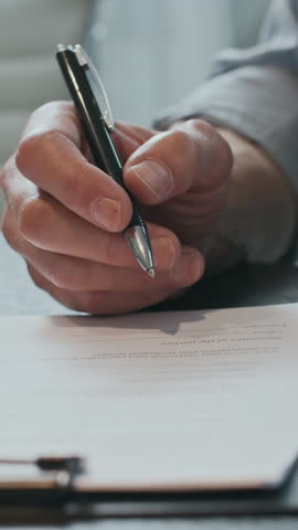 Vertical shot of hands of anonymous businessman signing contract at desk in office