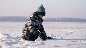 A child is kneeling on a snow-covered frozen lake, engaging in playful activities. The cold winter air is clear and crisp, creating a serene atmosphere around him. - Powered by Shutterstock - Get 15% off with code: PIKWIZARD15