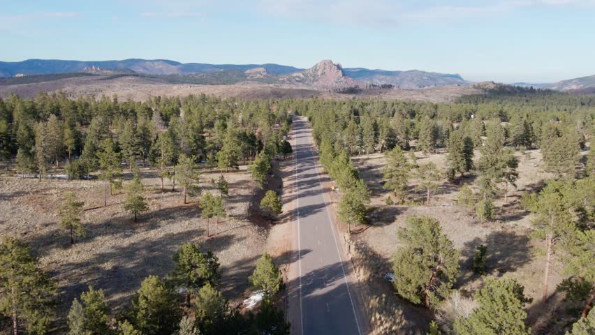 Aerial drone view of the Pike National Forest and a vehicle driving along a remote mountain highway. Forward dolly movement tracking a vehicle. Filmed in the Rocky Mountains of Colorado.
