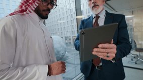 Handheld shot of Arab businessman talking to Caucasian male colleague holding digital tablet at modern office space - Powered by Shutterstock - Get 15% off with code: PIKWIZARD15