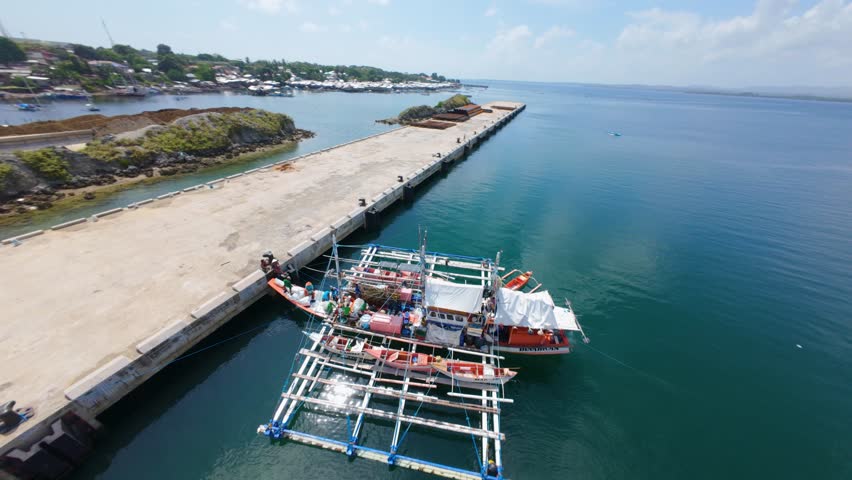 Aerial view of the new pier in Puerto Princesa, Palawan, showcasing docked vessels and a massive fishing banca with multiple smaller boats attached. The scene captures the busy maritime activity and t