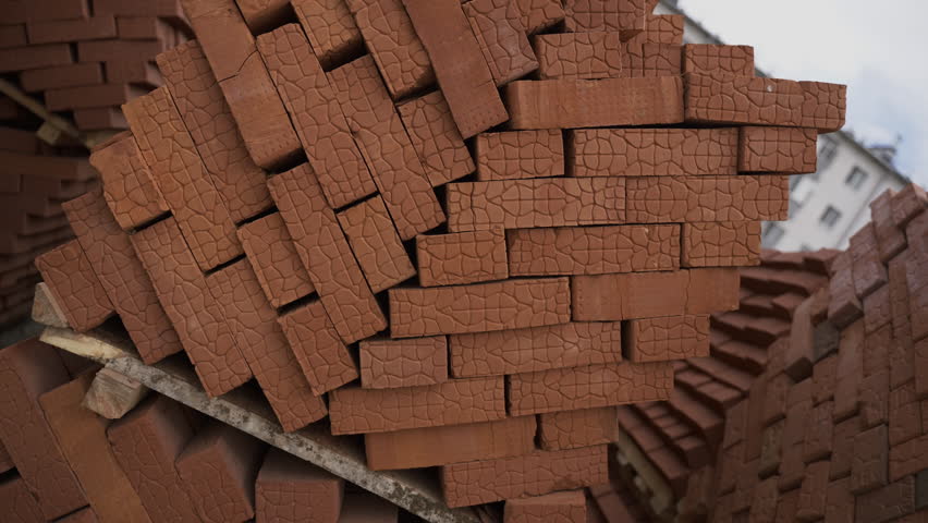 Stacks of red bricks arranged on wooden pallets at construction site. Construction materials form unusual pattern creating unique effect