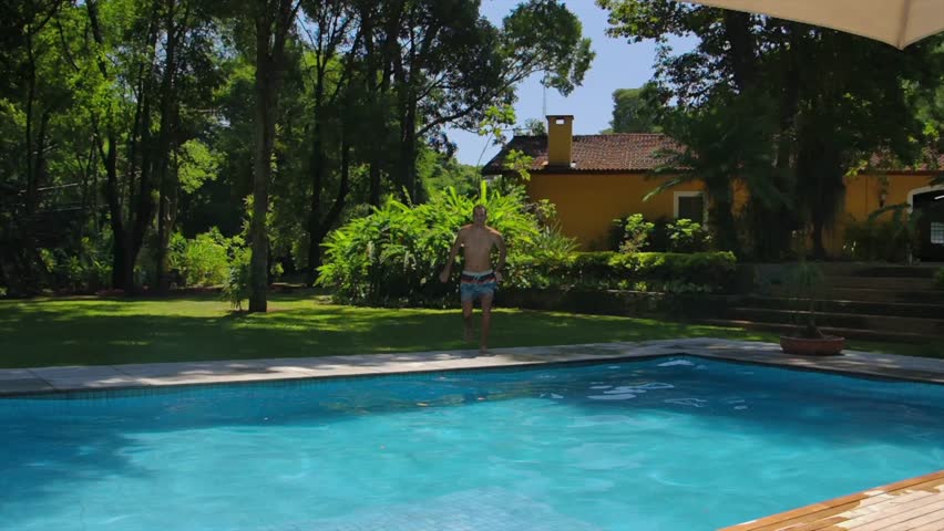 Man Jumping Into Swimming Pool At Resort In Summer. wide shot, slow motion