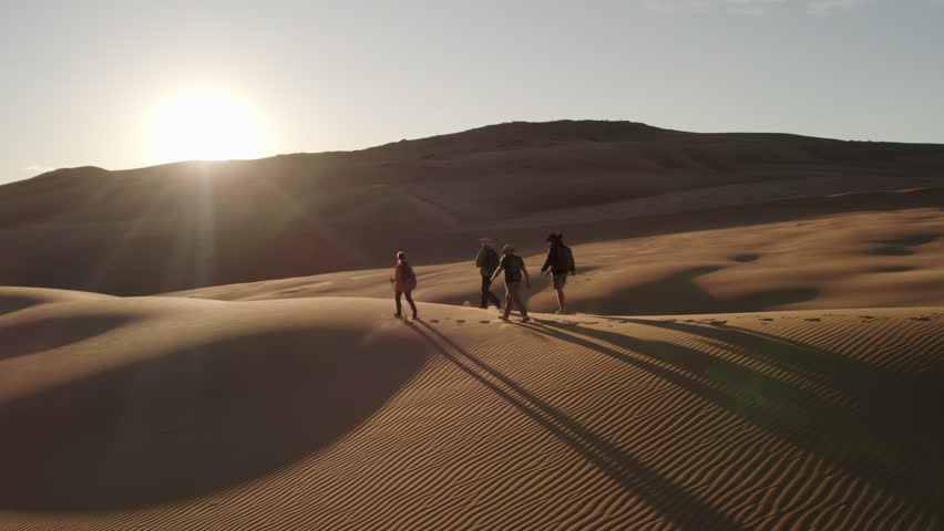 Group of a girl and three men walk along a dune in the Mongolian desert at sunset, long shadows, Mongol Els region