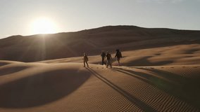 Group of a girl and three men walk along a dune in the Mongolian desert at sunset, long shadows, Mongol Els region - Powered by Shutterstock - Get 15% off with code: PIKWIZARD15