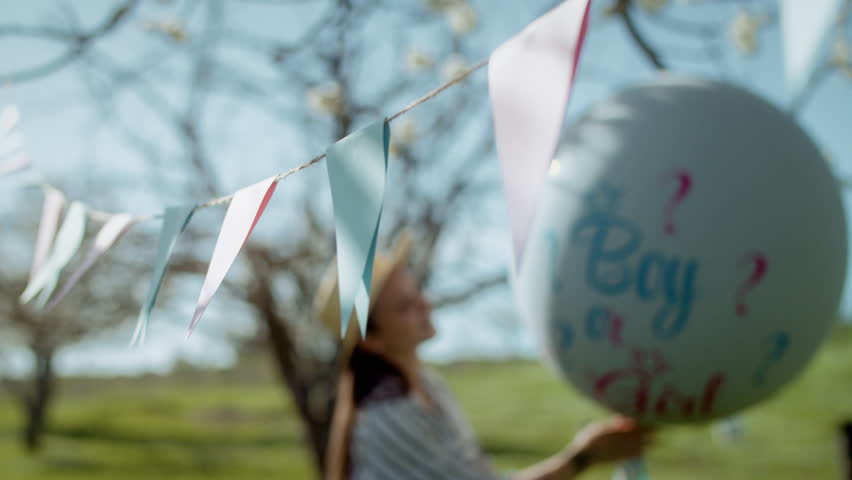 Decorations for a gender reveal party. Pregnant girl stands with a helium balloon with the inscription boy or girl. 4K slow motion
