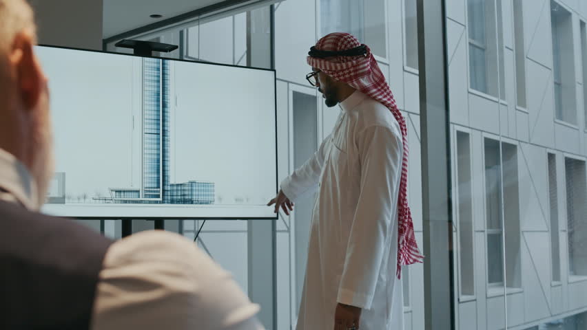 Over the shoulder view of male investor looking at Middle Eastern colleague giving presentation about architectural project at office