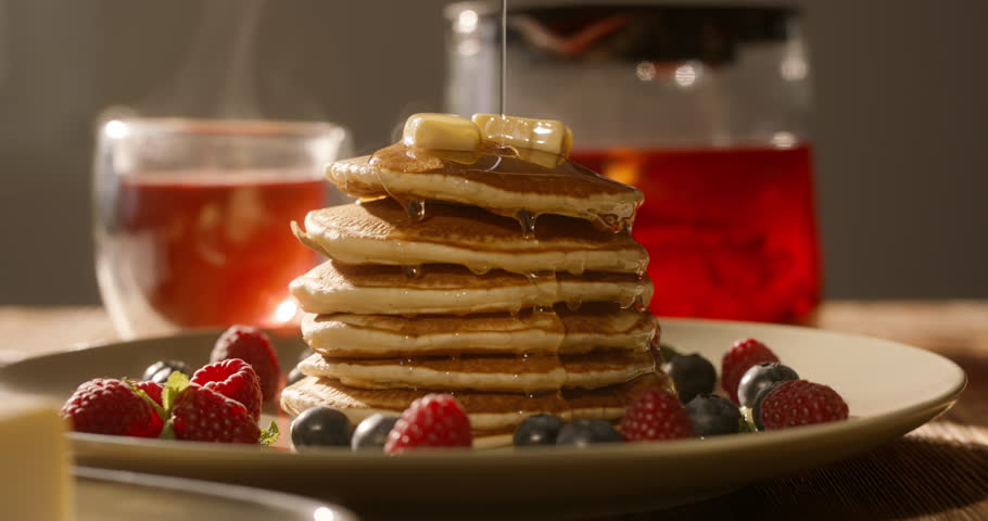Maple syrup syrup or honey pours in a thin stream onto the perfect tasty stack of pancakes. No people, advertising cinematic. Healthy lifestyle with individual approach to cooking and domestic life
