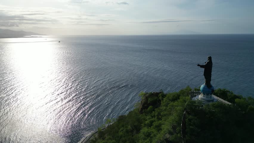 Aerial Drone View of Cristo Rei in Dili, the capital of Timor Leste, during a sunny day. Statue of Christ and beautiful beach, with clear blue water. RAW - no filter.