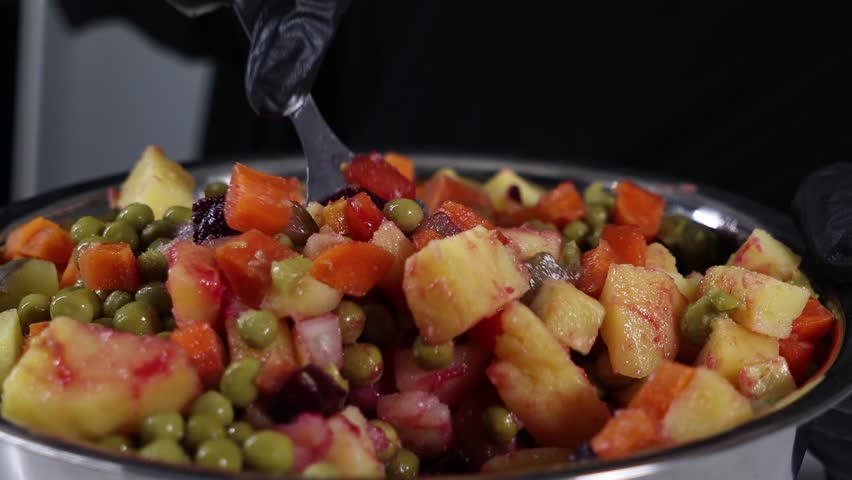 mixing traditional russian vinaigrette salad with diced vegetables, pickles, and green peas in a large metal bowl