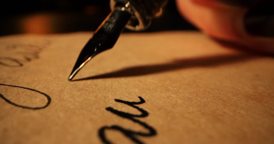 closeup of hand writing letter with vintage quill pen and ink on old parchment paper