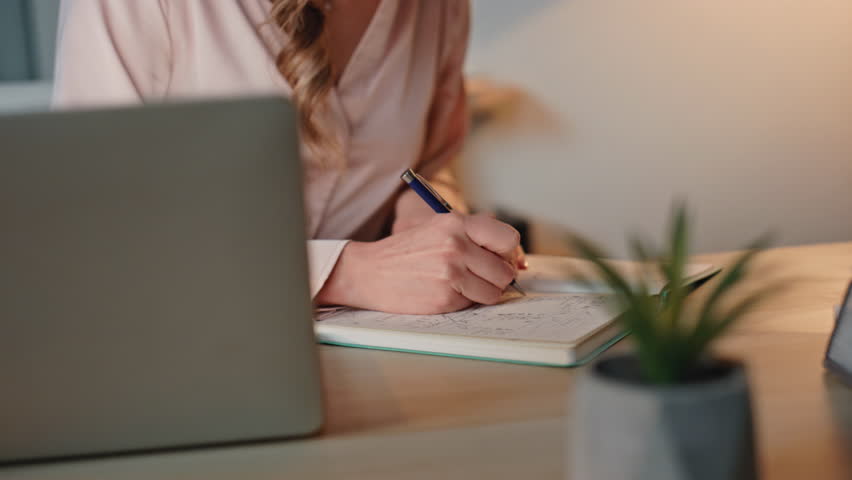 Closeup manager writing notes at buro. Smiling office lady working studying online at night. Joyful boss planning sales project in evening. Cheerful businesswoman making report reviewing documents