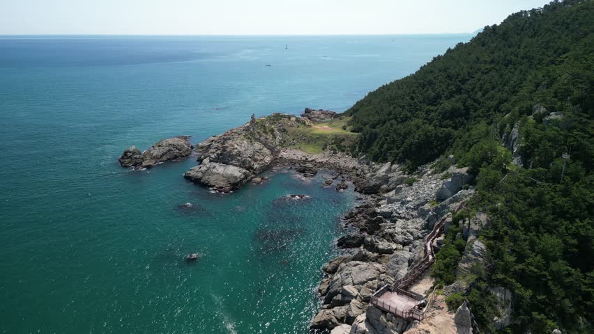 A drone footage of Haedong Yonggungsa Coast with blue sea, rocky shore and green hill on a sunny day in South Korea, Busan