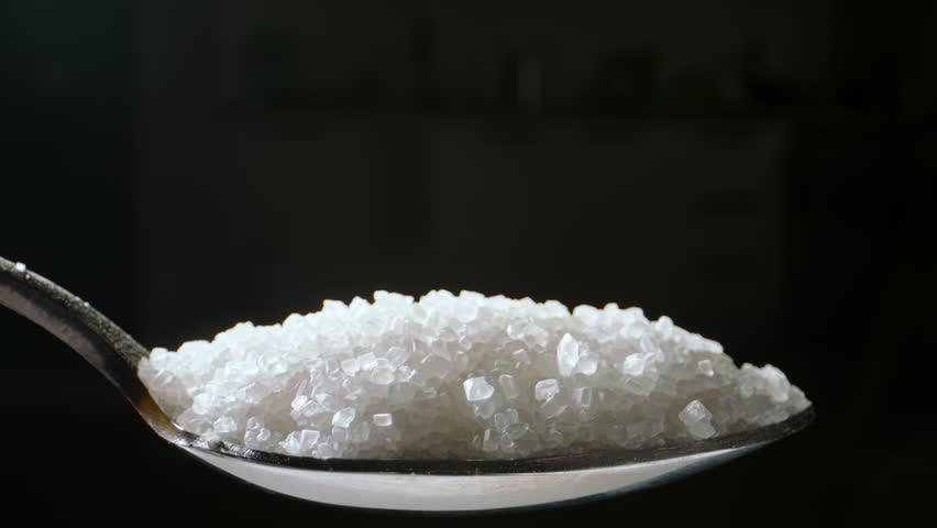 Spoon of white sugar. Close up slow motion black background. Behind allure of sugary treats lies an alarming reality: sugar can weaken our teeth, leading to dental decay and oral health issues. Diet