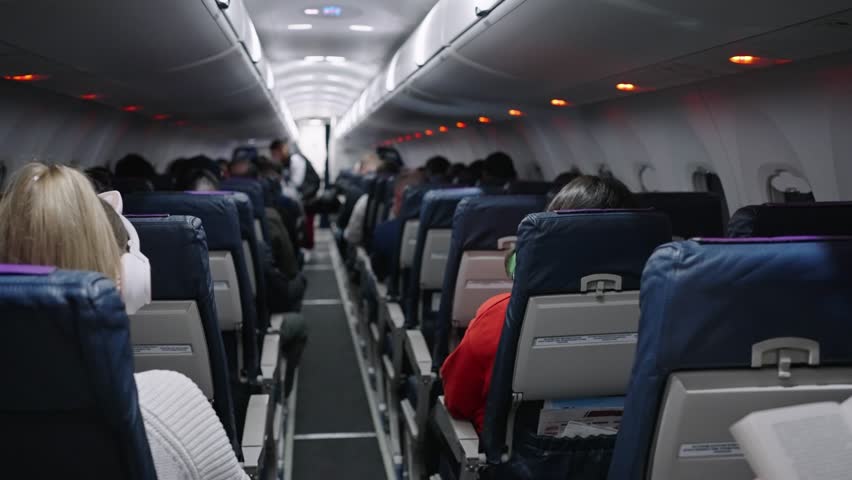 Airplane cabin interior revealing passengers seated during commercial flight, capturing economy class environment with overhead compartments and travelers occupying available seats