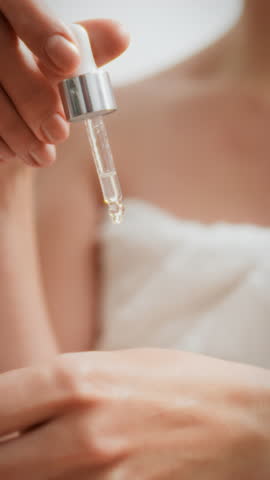 A woman uses a dropper to apply organic moisturizing lotion to her hand in a serene home spa setting. This moment emphasizes natural skin care and the importance of hydration