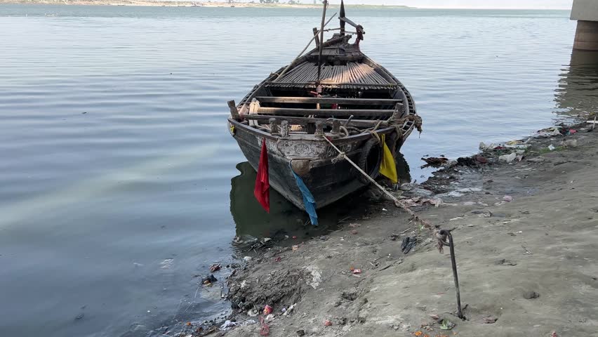 Closeup view of weathered wooden boat resting on a muddy shoreline, partially in the water in Ganga, Patna.