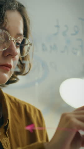 A medium business owner is focused on writing notes using a marker on a glass wall in a corporate office. This creative activity occurs during a brainstorming session to generate ideas