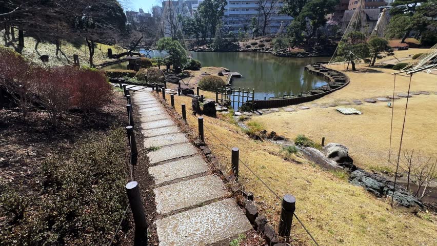 A peaceful park in Tokyo featuring a pond, walking path, and modern buildings nearby