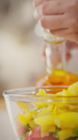 A housewife is having fun preparing a fresh salad at the kitchen table, drizzling olive oil over colorful vegetables. The kitchen is bright, showcasing a joyful cooking atmosphere