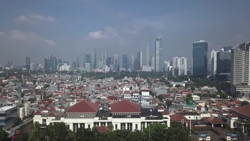 An aerial view of Jakarta’s dense residential area, showcasing a mix of traditional houses and modern high-rise buildings. The urban sprawl of Indonesia’s capital city highlights rapid development and